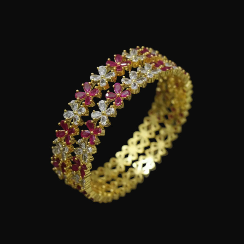 Gold bangles with pink stones on a dark background, branded 'Saheli'.