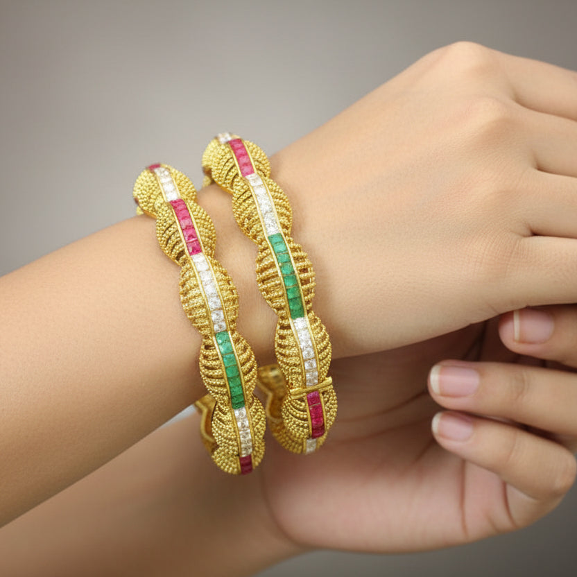 Gold bangles with green and red stones on a gray background, featuring the brand 'Saheli'.