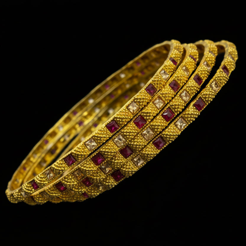 Gold bangles with red stones on a dark background, featuring the brand 'Saheli'.