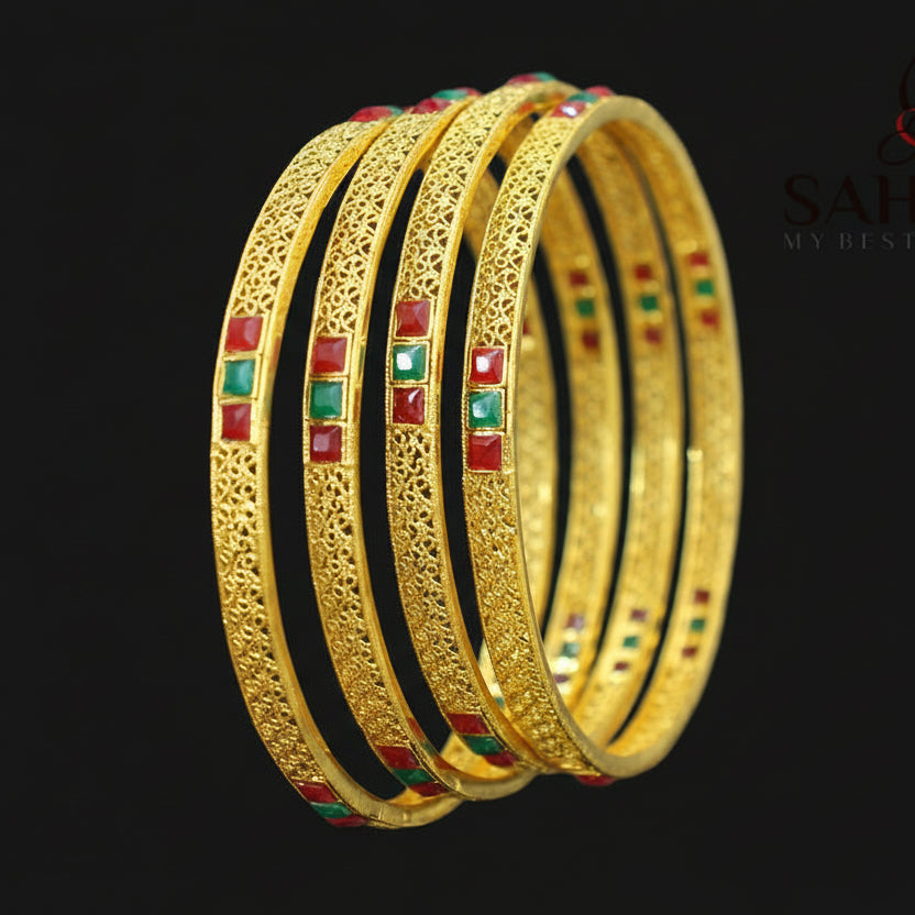 Gold bangles with red and green stones on a dark background, featuring the brand 'Saheli'.