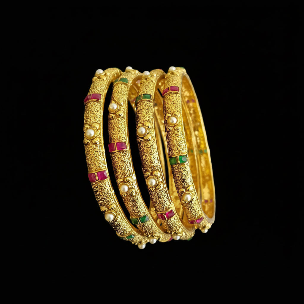 Set of gold bangles with gemstones on a gray background, featuring the brand 'SAHELI'.