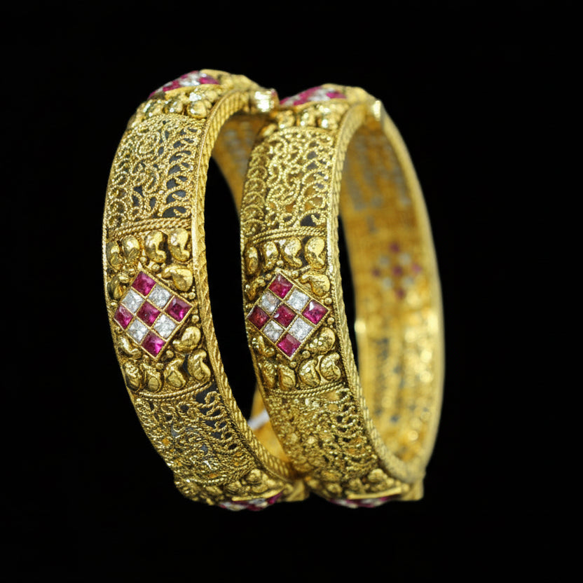 Gold bangles with red gemstones on a gray background, featuring the brand 'Saheli'.
