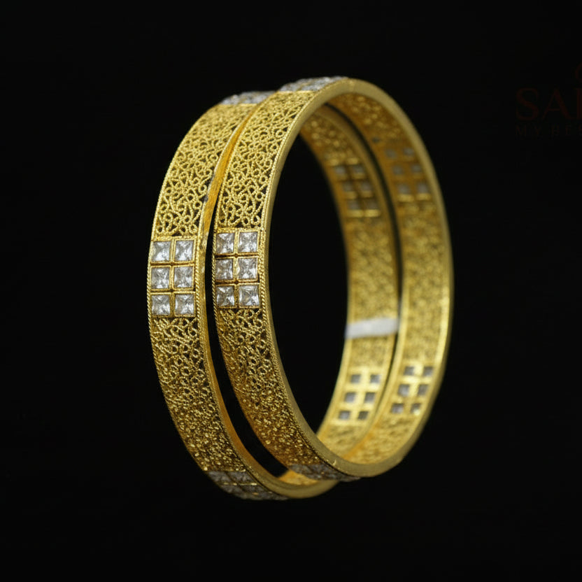 Gold bangles with intricate designs on a dark background, featuring the brand 'Saheli'.