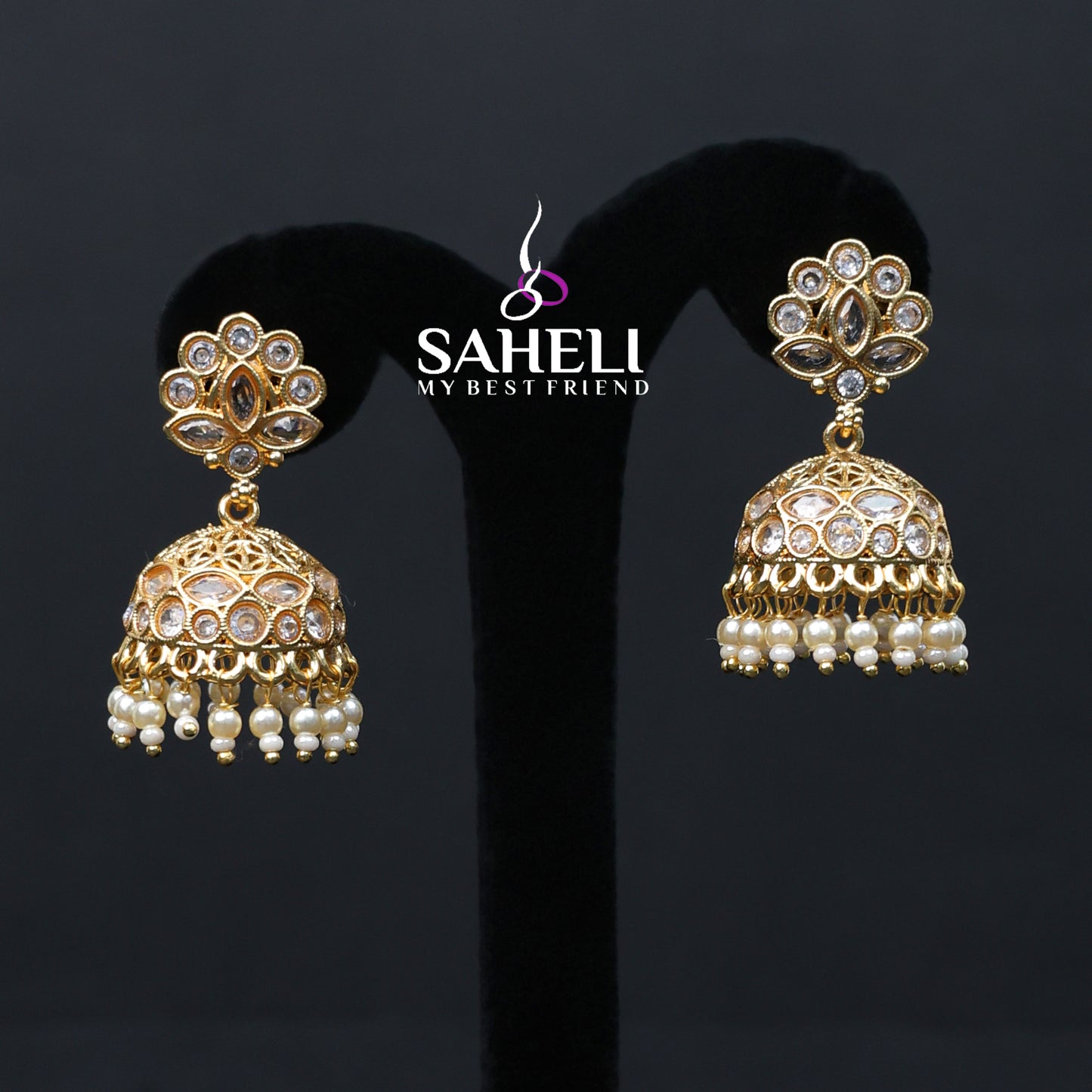 Gold and pearl earrings on a black stand with 'SAHELI' branding.