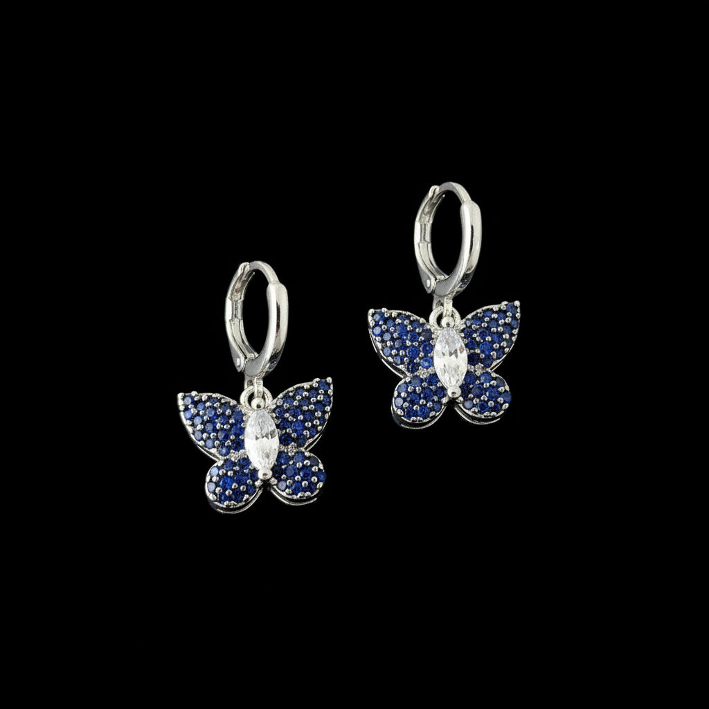 Butterfly-shaped earrings with blue gemstones on a dark background, branded 'Saheli'.