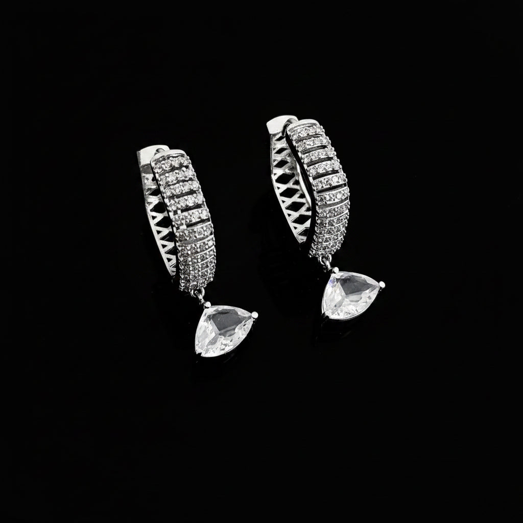 Silver hoop earrings with teardrop-shaped gemstones on a dark background, featuring the brand 'Saheli'.