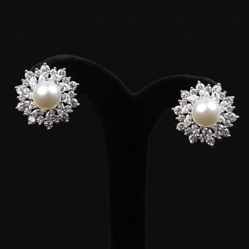 Pearl earrings with diamond accents on a black stand, branded 'Saheli'.