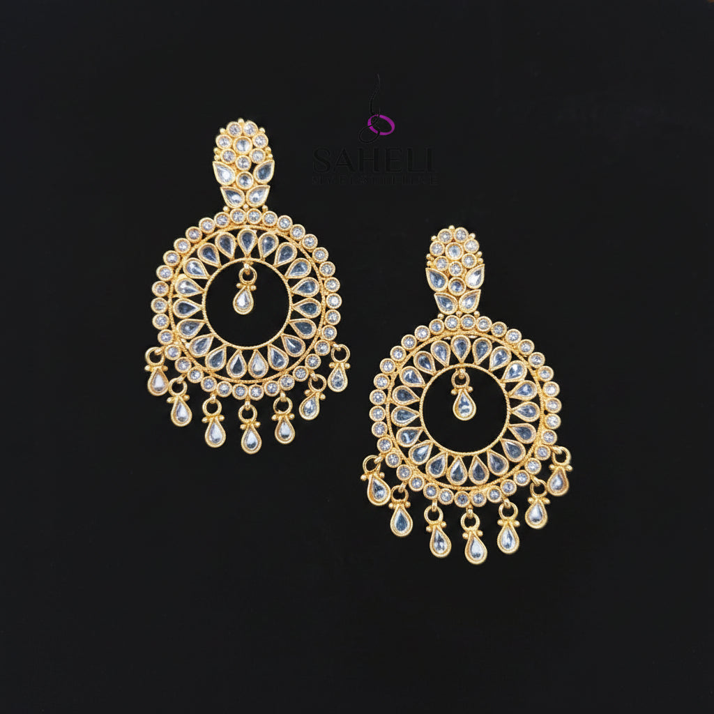A pair of gold-toned Indian chandelier earrings with clear teardrop crystals, displayed on a black background with the SAHeli Jewellers logo above.
