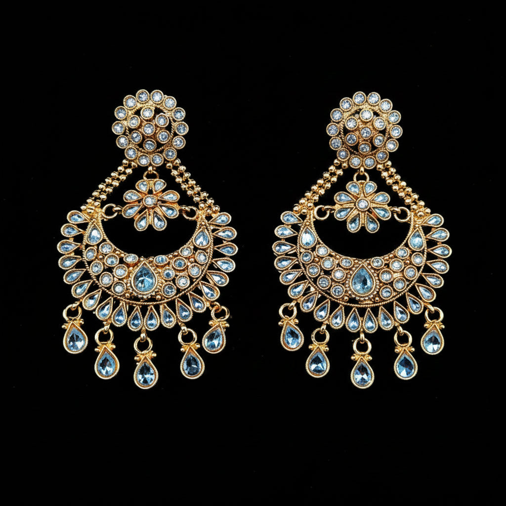 A pair of gold-toned traditional Indian chandelier earrings adorned with light blue and clear stones, displayed against a solid black background with a purple 'SAHELI MY BEST FRIEND' logo at the top.