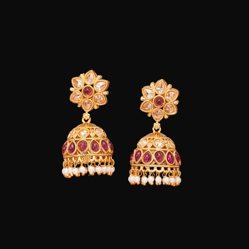 Pair of gold earrings with red and white stones on a brown background