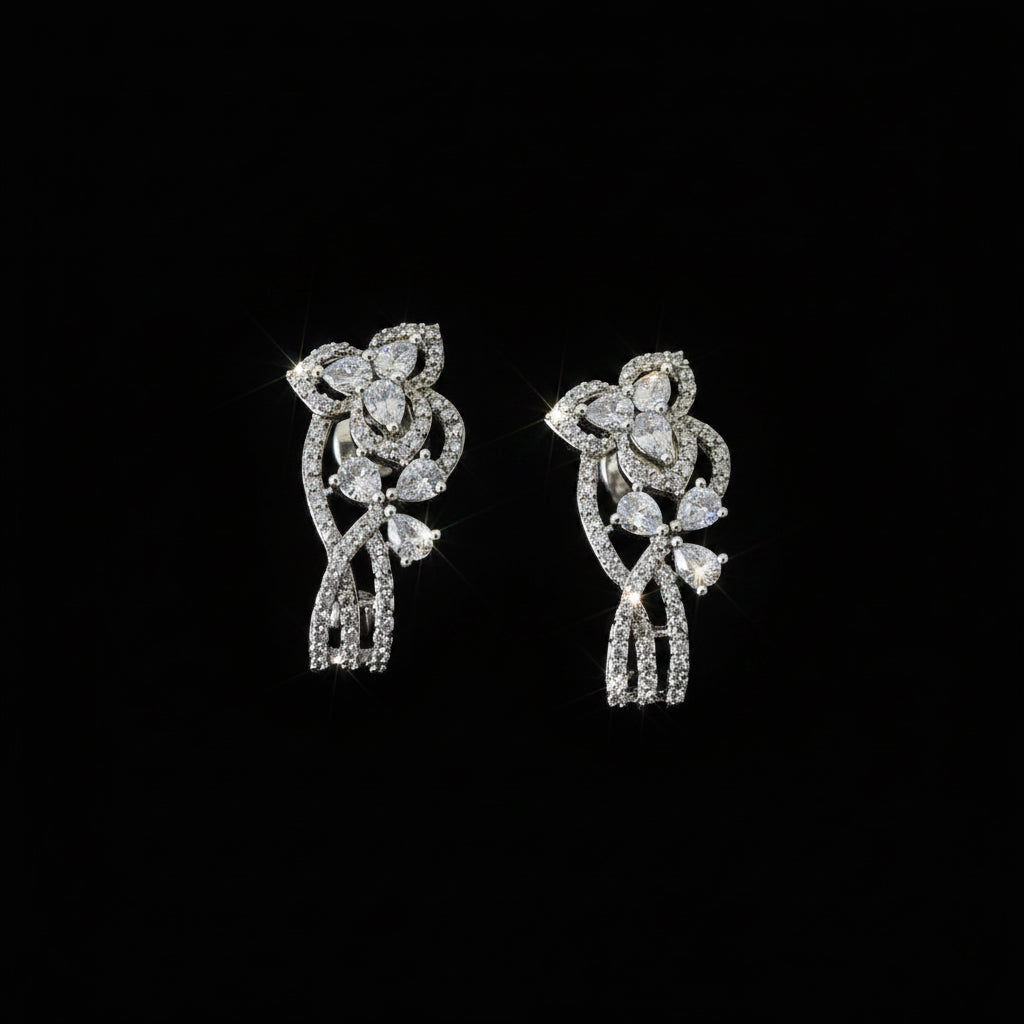 Silver floral earrings on a dark stand with 'SAHELI' branding.