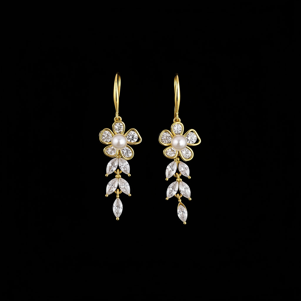 A pair of gold flower drop earrings with clear rhinestones and a central pearl, displayed on a teal background with decorative stones.