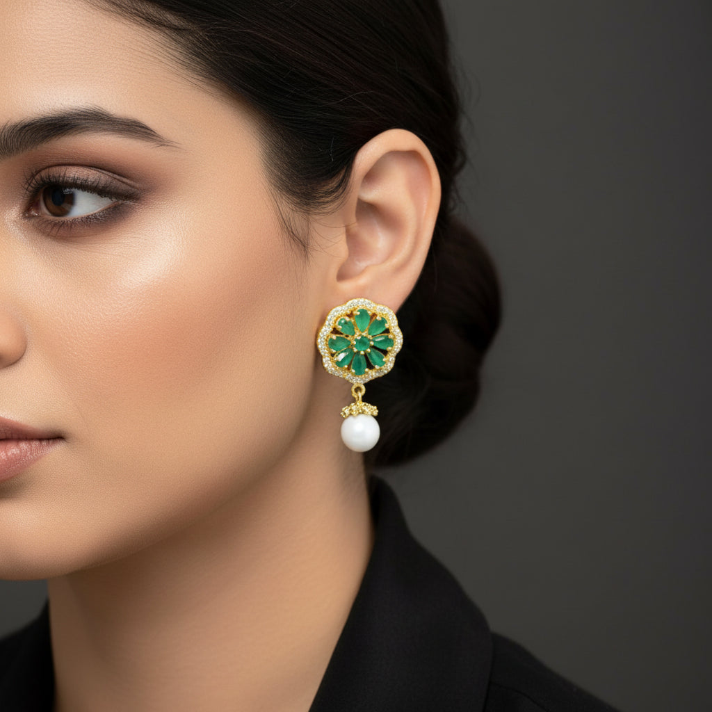 Gold earrings with green gemstones and white beads on a gray background, branded 'SAHELI'.