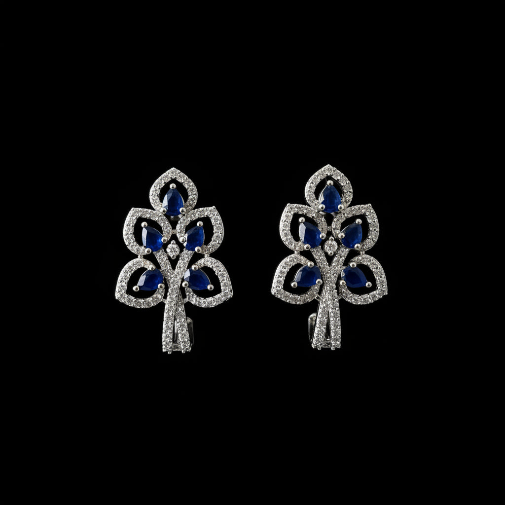 Silver earrings with blue gemstones on a dark background, featuring the brand 'Saheli'.