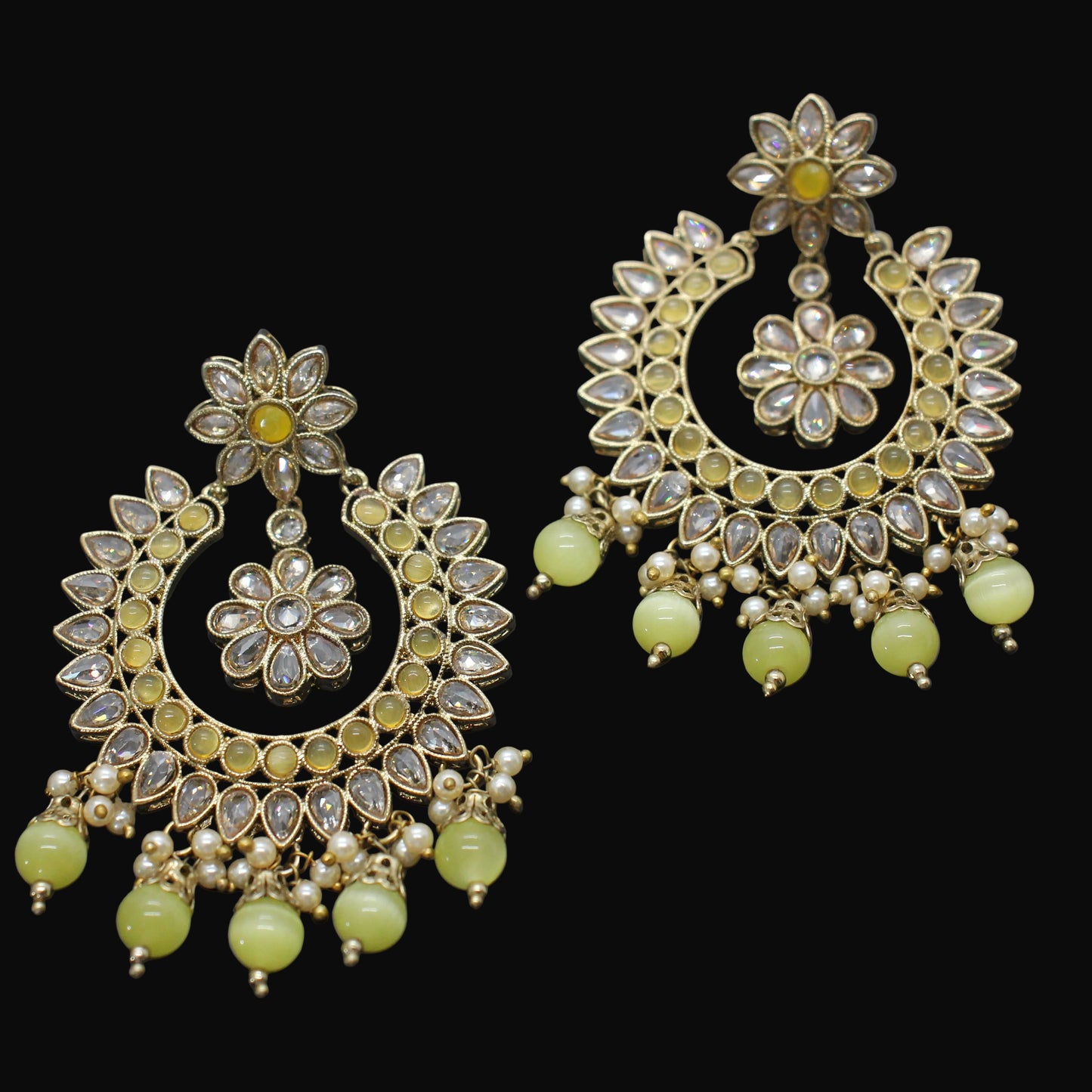Pair of ornate earrings with floral designs and green beads on a dark background
