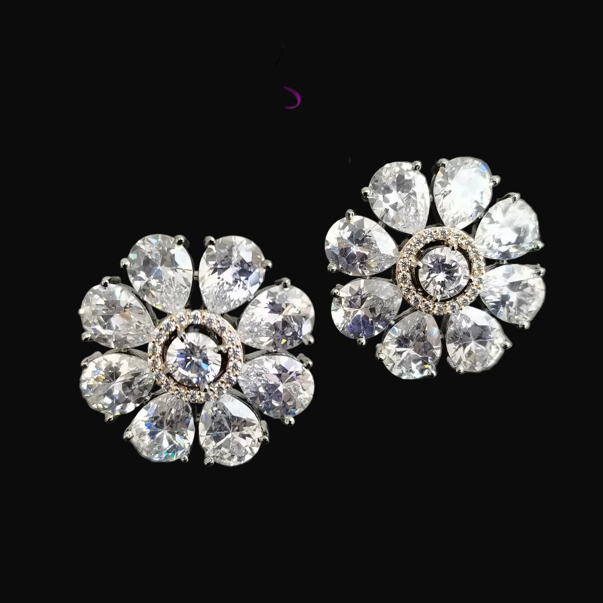 Pair of silver floral earrings with clear gemstones on a gray background, branded 'Saheli'.