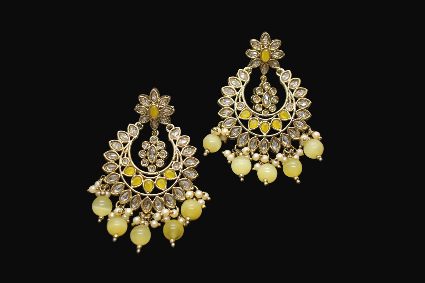 Pair of ornate earrings with yellow beads on a gray background