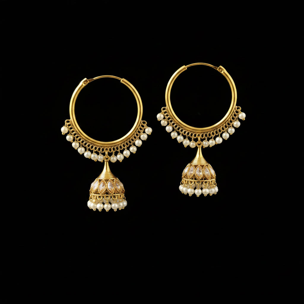 A pair of gold-plated Indian jhumka earrings with white pearl bead borders and dangling bell-shaped charms, displayed on a gray jewelry stand.
