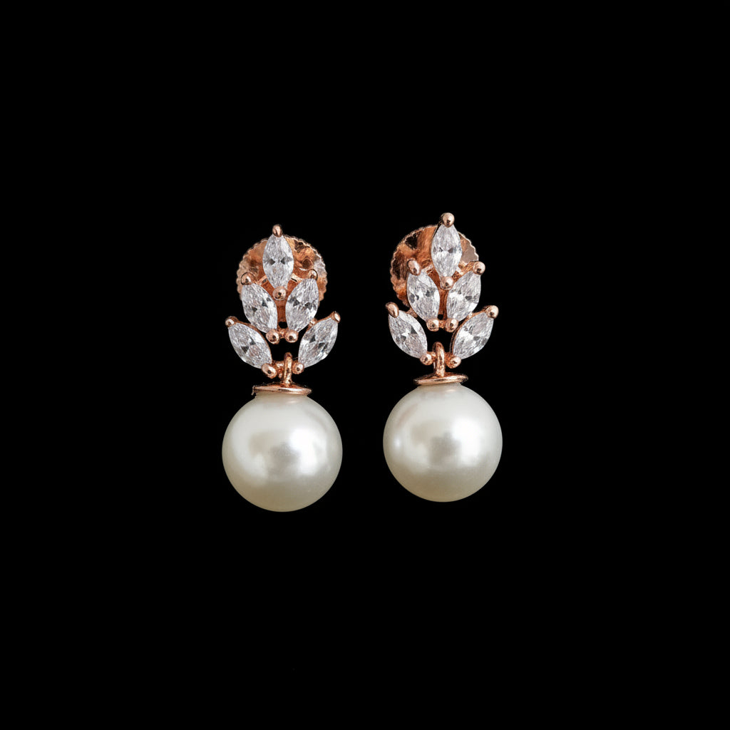 A pair of rose gold drop earrings with marquise-cut clear crystals arranged in a leaf-like cluster above a large white pearl, displayed on a black stand against a dark gray background.