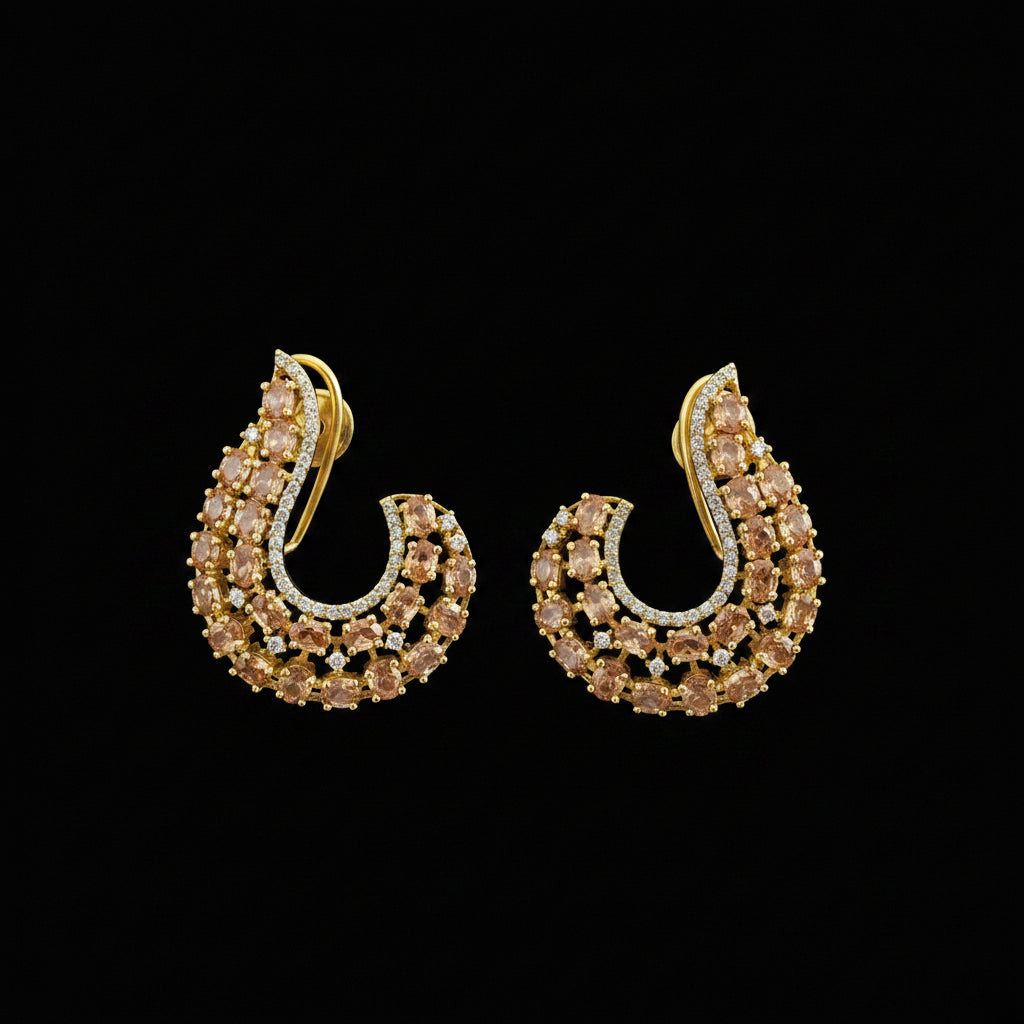 A pair of gold-toned crescent-shaped earrings embellished with small clear stones and accented with warm yellow stones, displayed on a dark reflective surface with the SAHELI MY BEST FRIEND logo above.