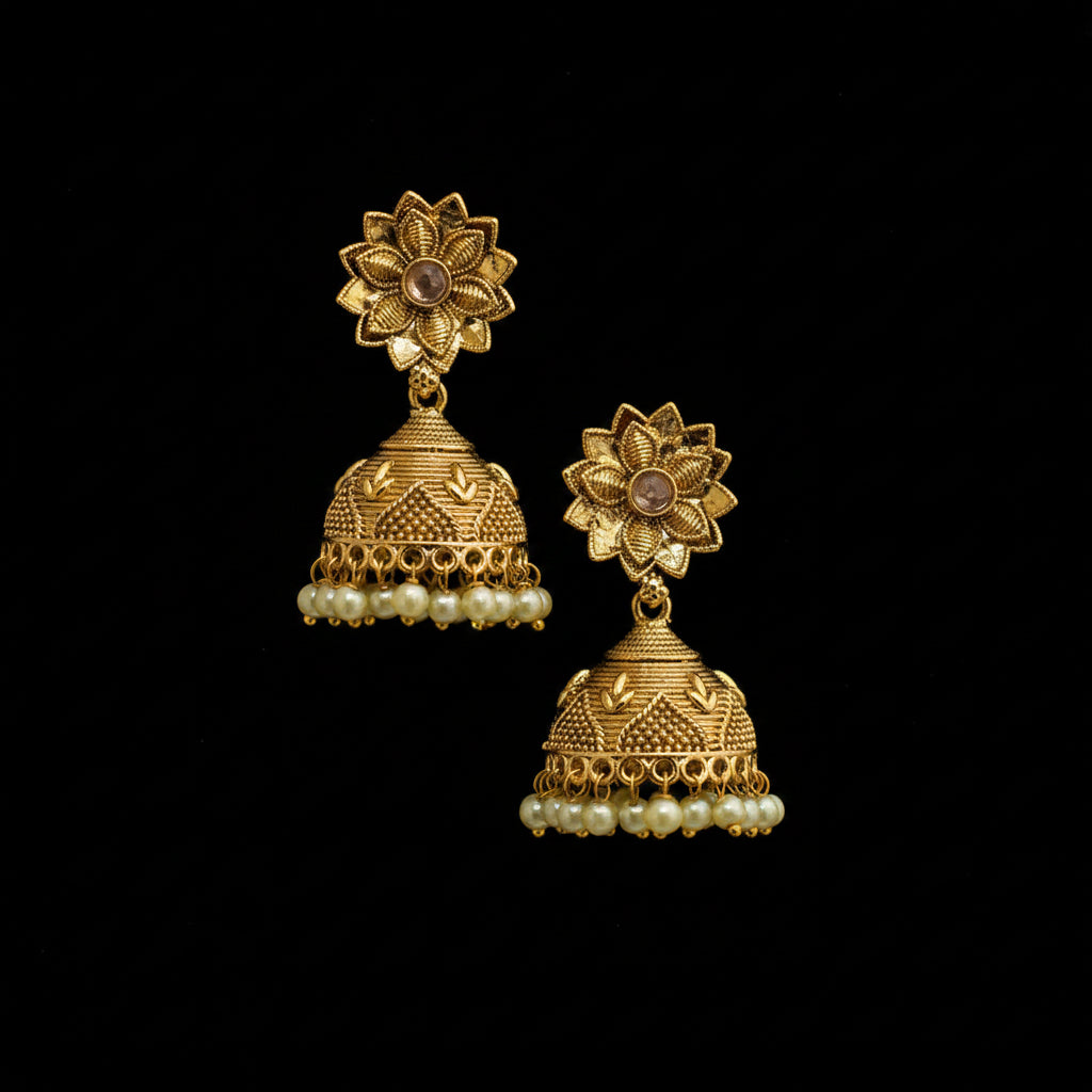 Gold earrings with floral design and pearl details on a black stand against a dark background