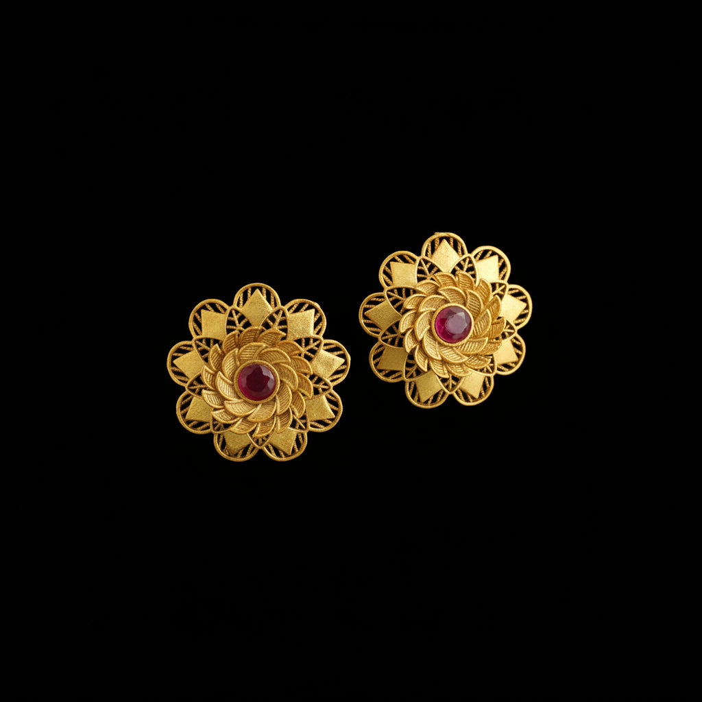 Pair of gold flower-shaped earrings with red centers on a dark background