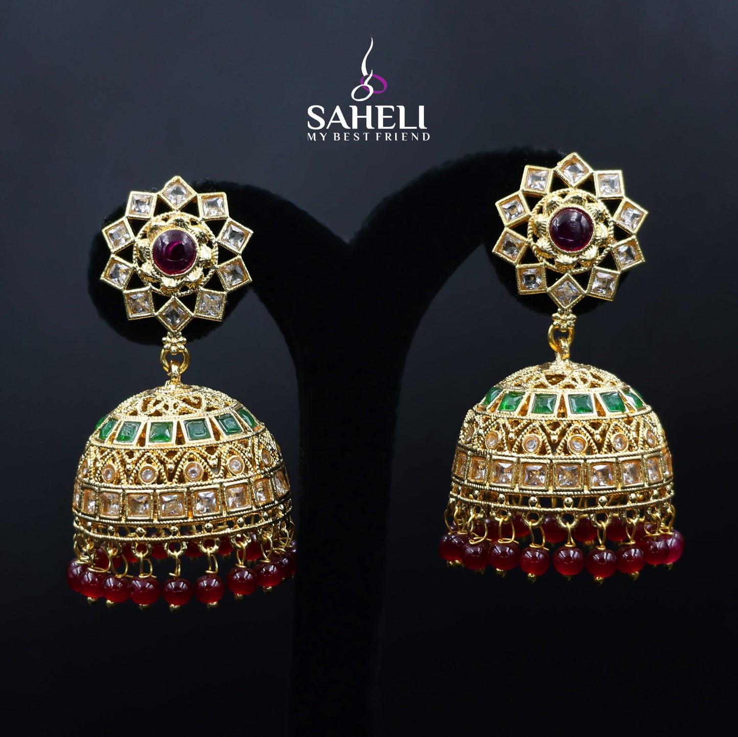 Ornate gold earrings with gemstones on a dark background, featuring the brand 'Saheli'.