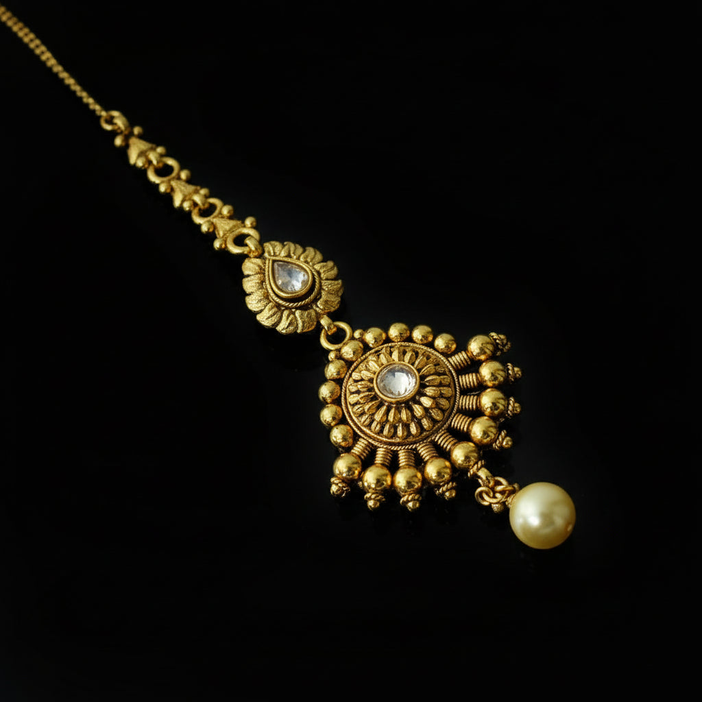 Gold necklace with decorative elements and a pearl on a gray background, branded 'Saheli'.