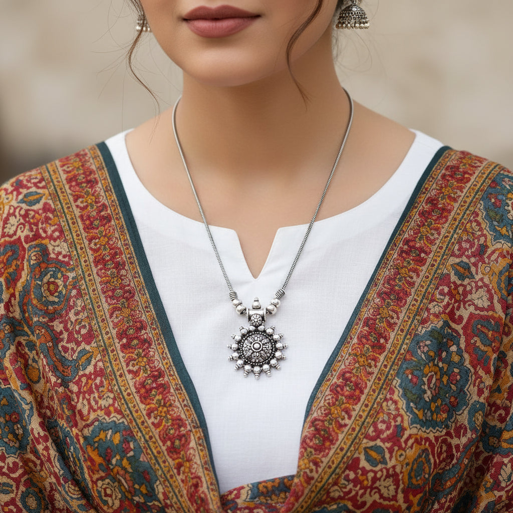 Silver necklace with a detailed pendant on a gray background, featuring the brand 'SAHELI'.