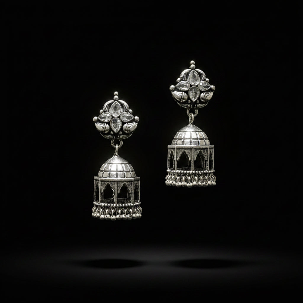 Pair of silver jhumka earrings on a black stand against a gray background