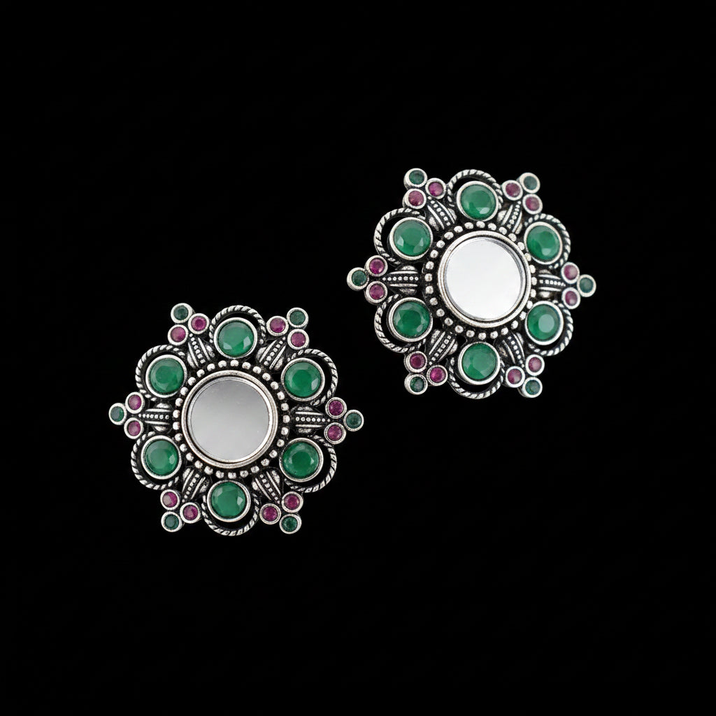 Pair of silver earrings with green and pink gemstones on a gray background