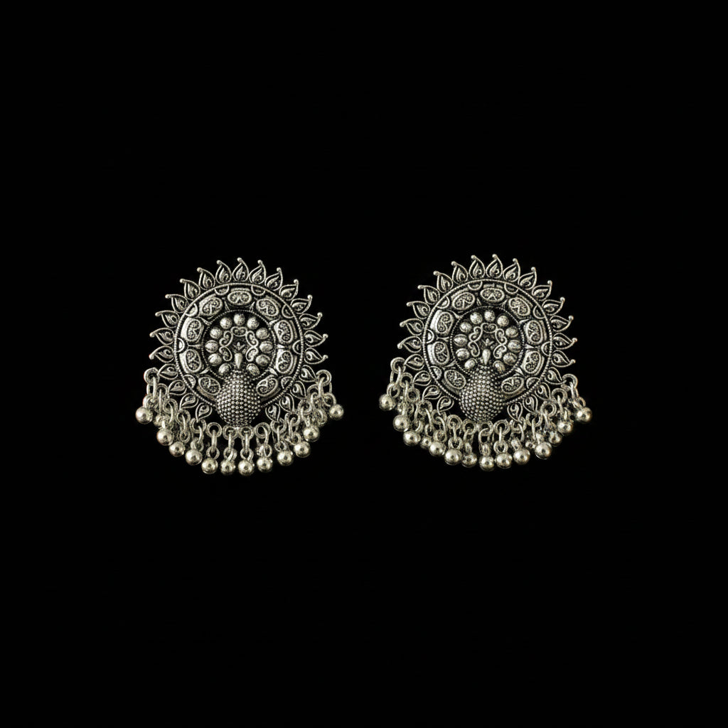 A pair of ornate silver-toned Indian jhumka earrings with intricate filigree work, floral motifs, and dangling bead chains, displayed on a dark reflective surface.