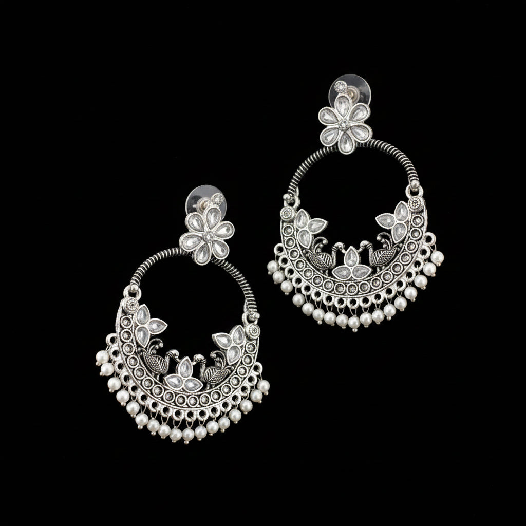 Pair of silver earrings with floral designs on a dark background