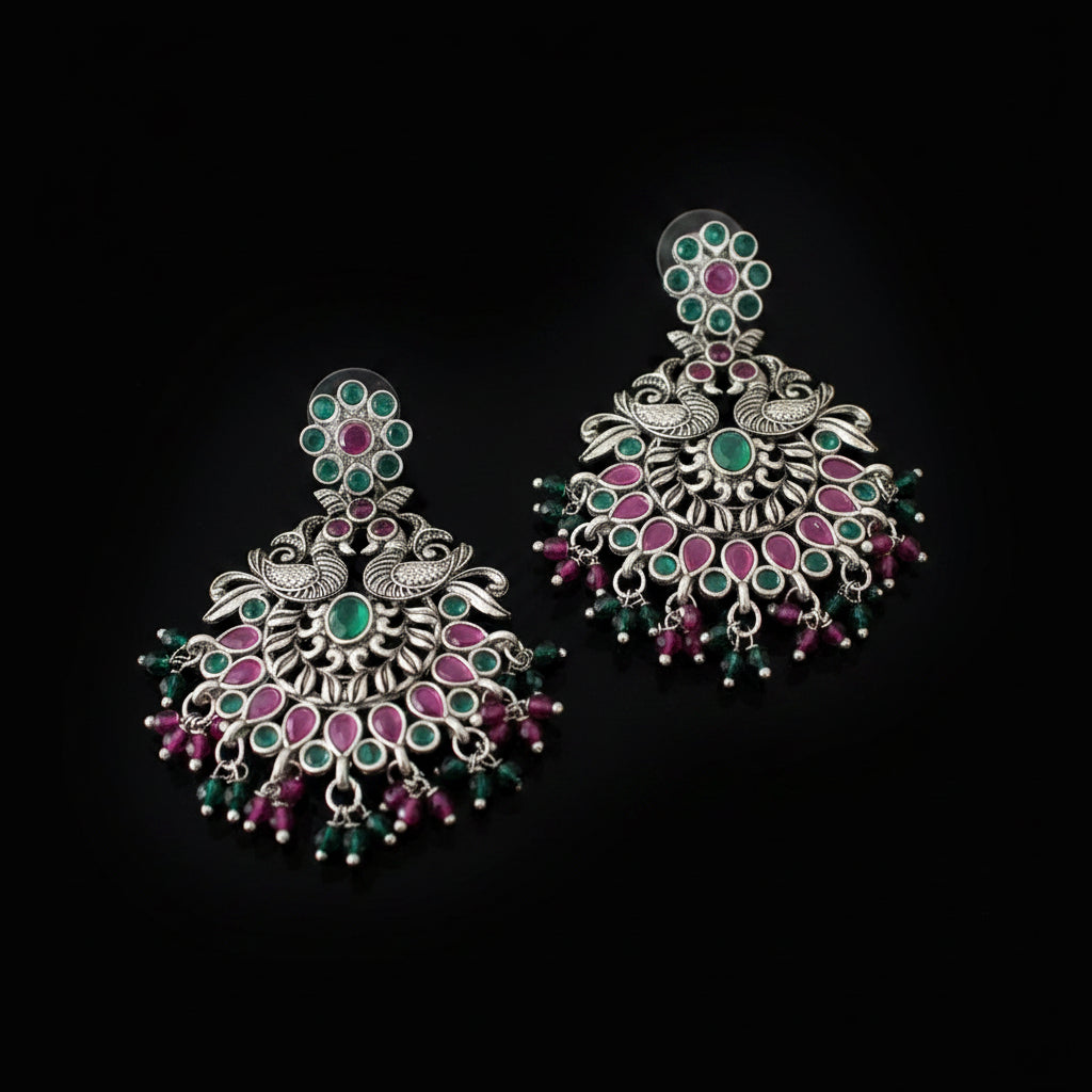 Pair of silver earrings with green and pink stones on a gray background