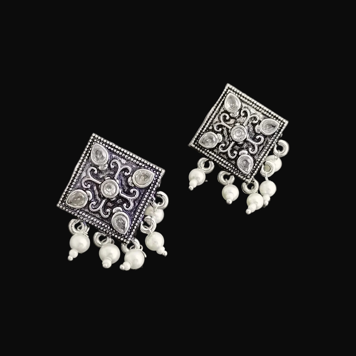 Pair of silver earrings with square designs and pearl-like beads on a dark background