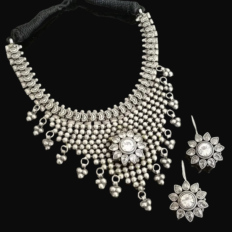 Silver necklace and earrings set with 'Saheli' branding on a gray background
