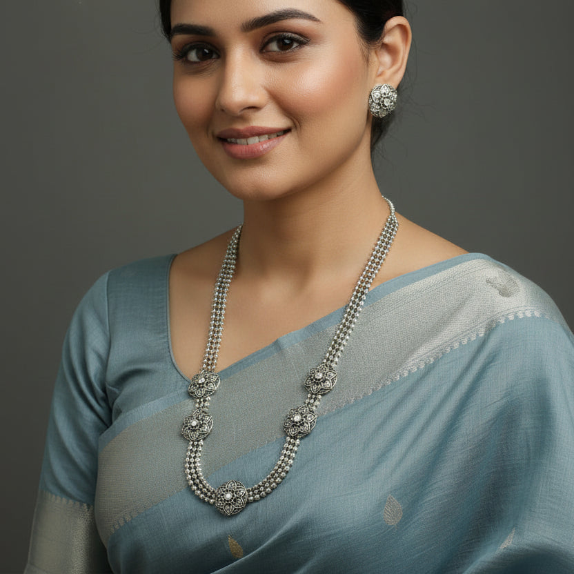 Silver necklace with floral designs and green gemstones on a black background