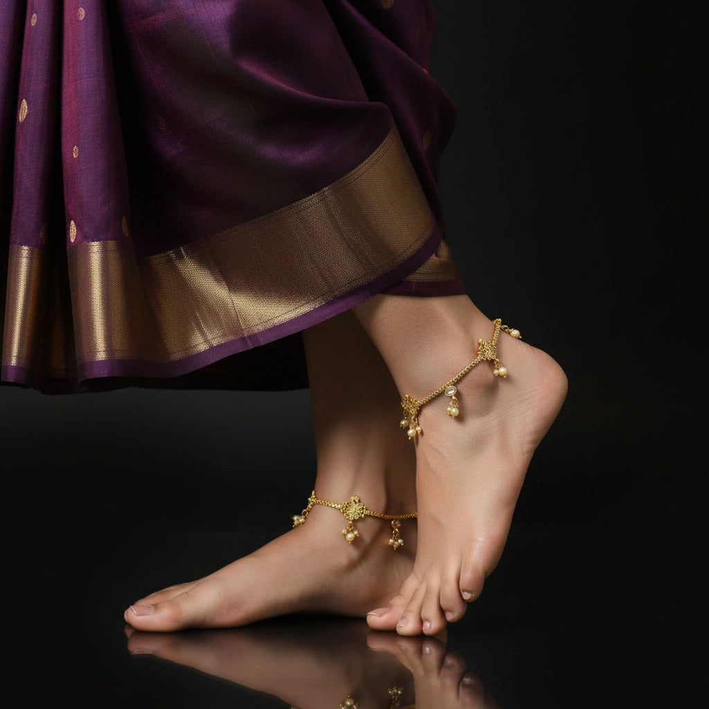 Gold anklets on a foot with a purple saree against a black background