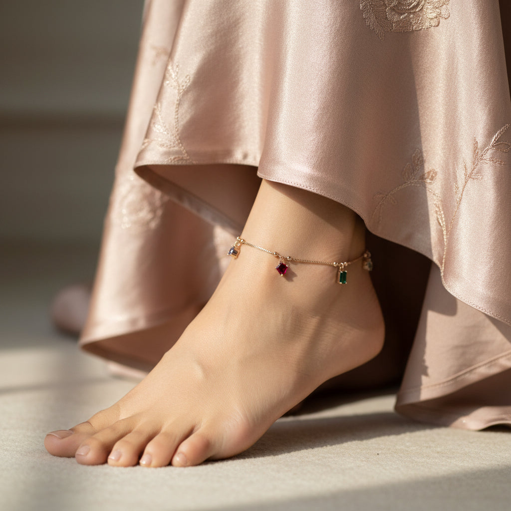 Gold anklet with colorful stones on a dark background, featuring the brand 'Saheli'.