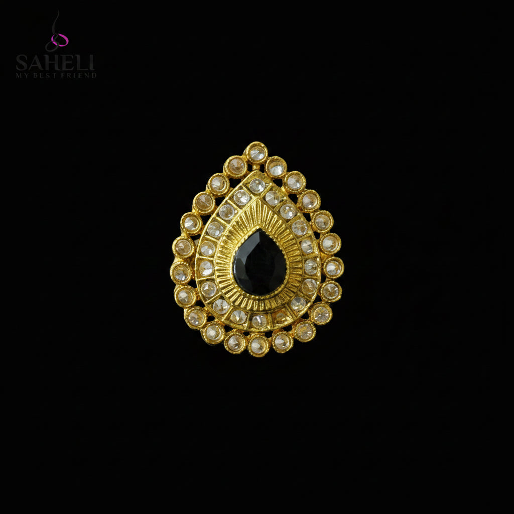 A gold teardrop-shaped traditional Indian jewelry piece featuring a central black teardrop stone surrounded by clear stones, displayed on a dark gray background with a SAHELL MY BEST FRIEND logo in the top left corner.