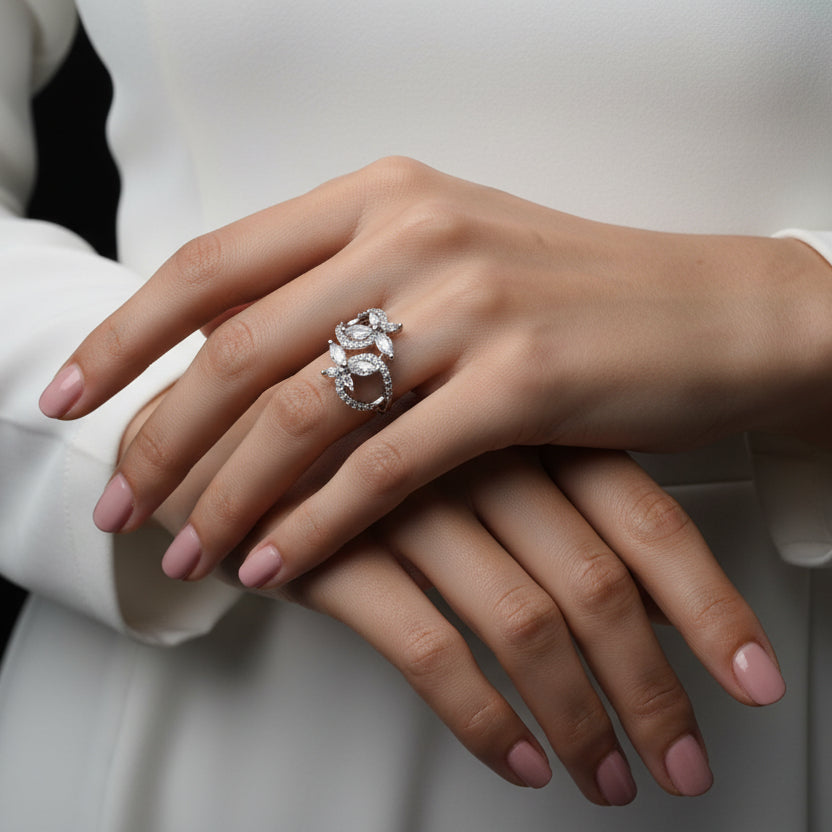 Silver leaf-shaped earrings on a black glove with 'SAHELI' branding.