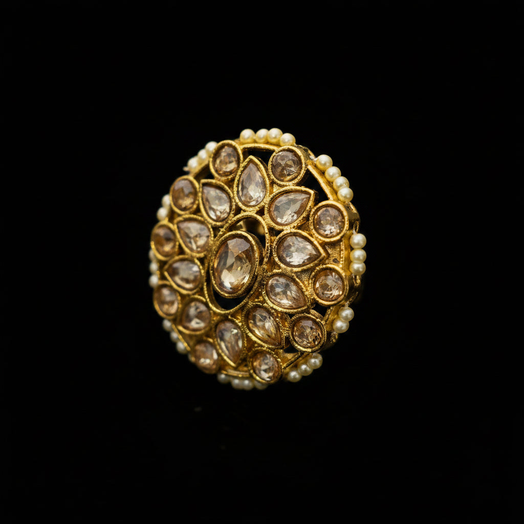 A gold-toned traditional Indian Kundan ring featuring a circular floral pattern set with clear stones and bordered by small white pearls, displayed on a dark reflective surface.