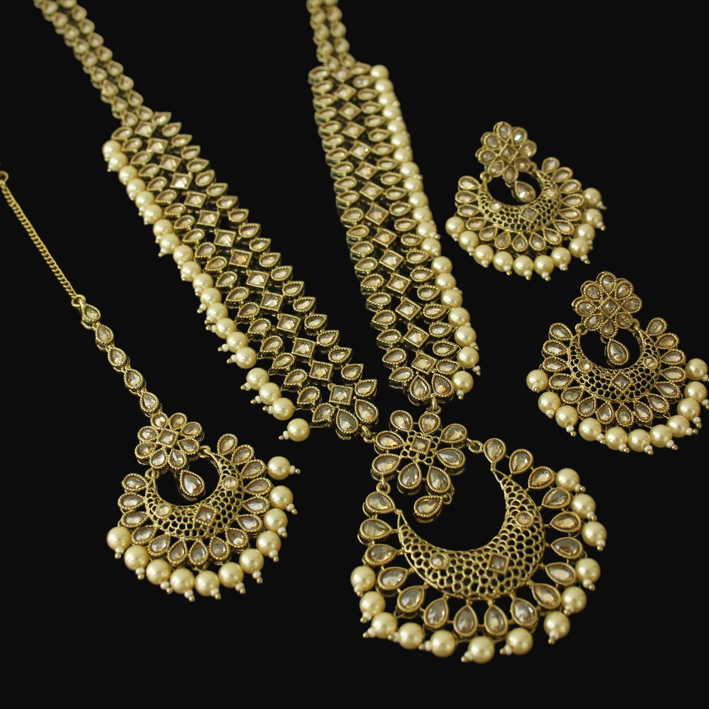 Set of gold jewelry including necklace, earrings, and hair accessories on a dark background