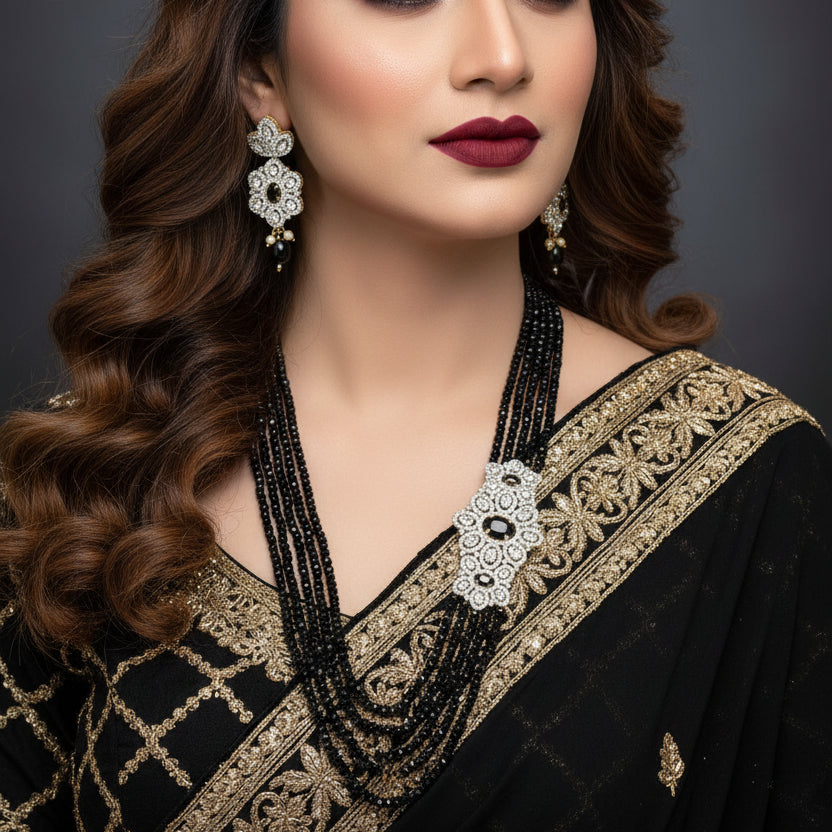 Black beaded necklace with floral designs and matching earrings on a gray background, featuring the brand 'SAHELI'.