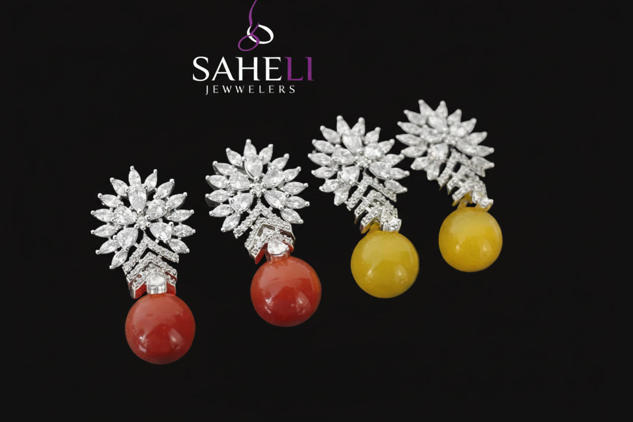 Four earrings with star-shaped tops and colored beads on a dark surface, branded 'Saheli'.