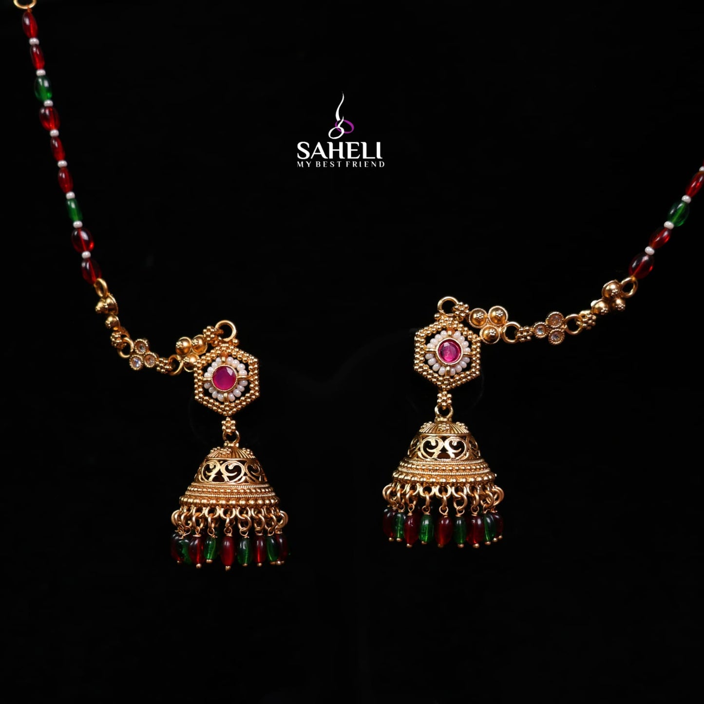 Gold necklace with jhumka earrings on a black background, featuring the brand 'Saheli'.