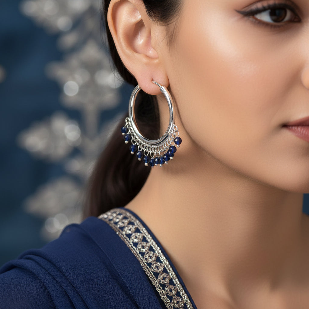Pair of silver hoop earrings with blue beads on a brown background