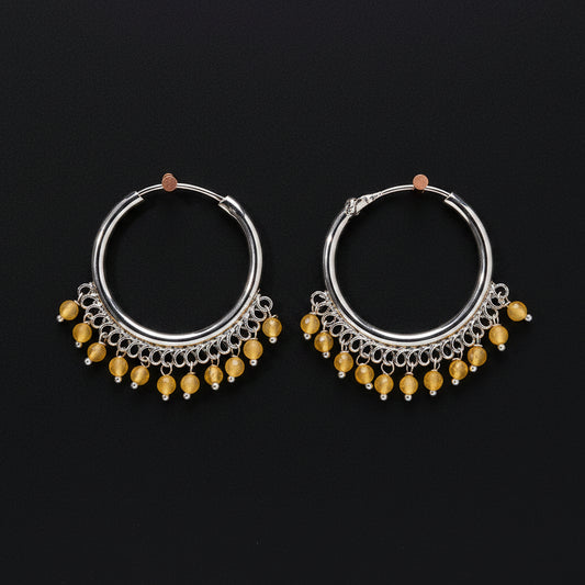 Pair of silver hoop earrings with yellow beads on a brown background