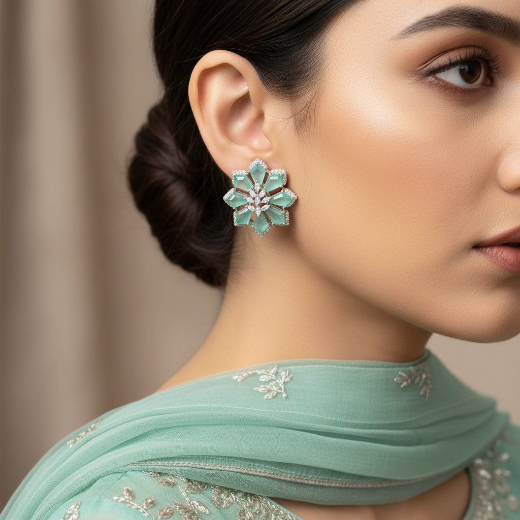 Pair of snowflake-shaped earrings with green gemstones on a pink background