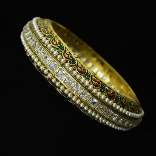 Decorative gold bracelet with gemstones on a reflective surface, branded 'Saheli'.